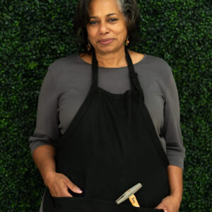 Amy is a Black female wearing a gray shirt and black apron with a hammer.