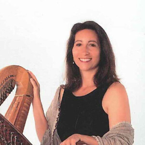 Andrea is a white woman in a black dress holding two harps.