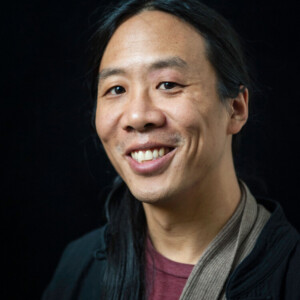 Andrew is an Asian male wearing a red shirt and black jacket.