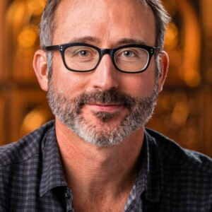 Deacon is a white male wearing glasses and a blue and black plaid shirt.