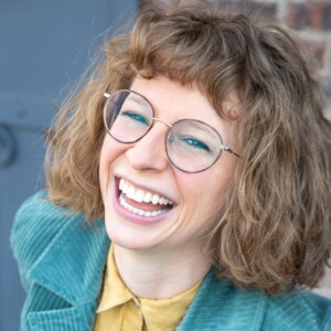 Julia is a white female wearing a yellow shirt and blue jacket.