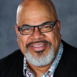 T. Mychael is a black man wearing a plaid shirt under a black shirt.