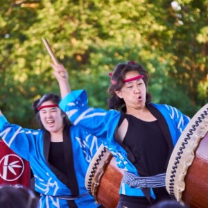 The TaikoArts Midwest performers are wearing black shirts under blue robes.