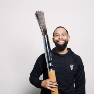 Broderick is a Black male wearing a black shirt and holding a glue brush.